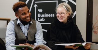Kaksi nuorta istuu ja hymyilee. Käsissään vihkoset. Takana Business Lab -seinäke.