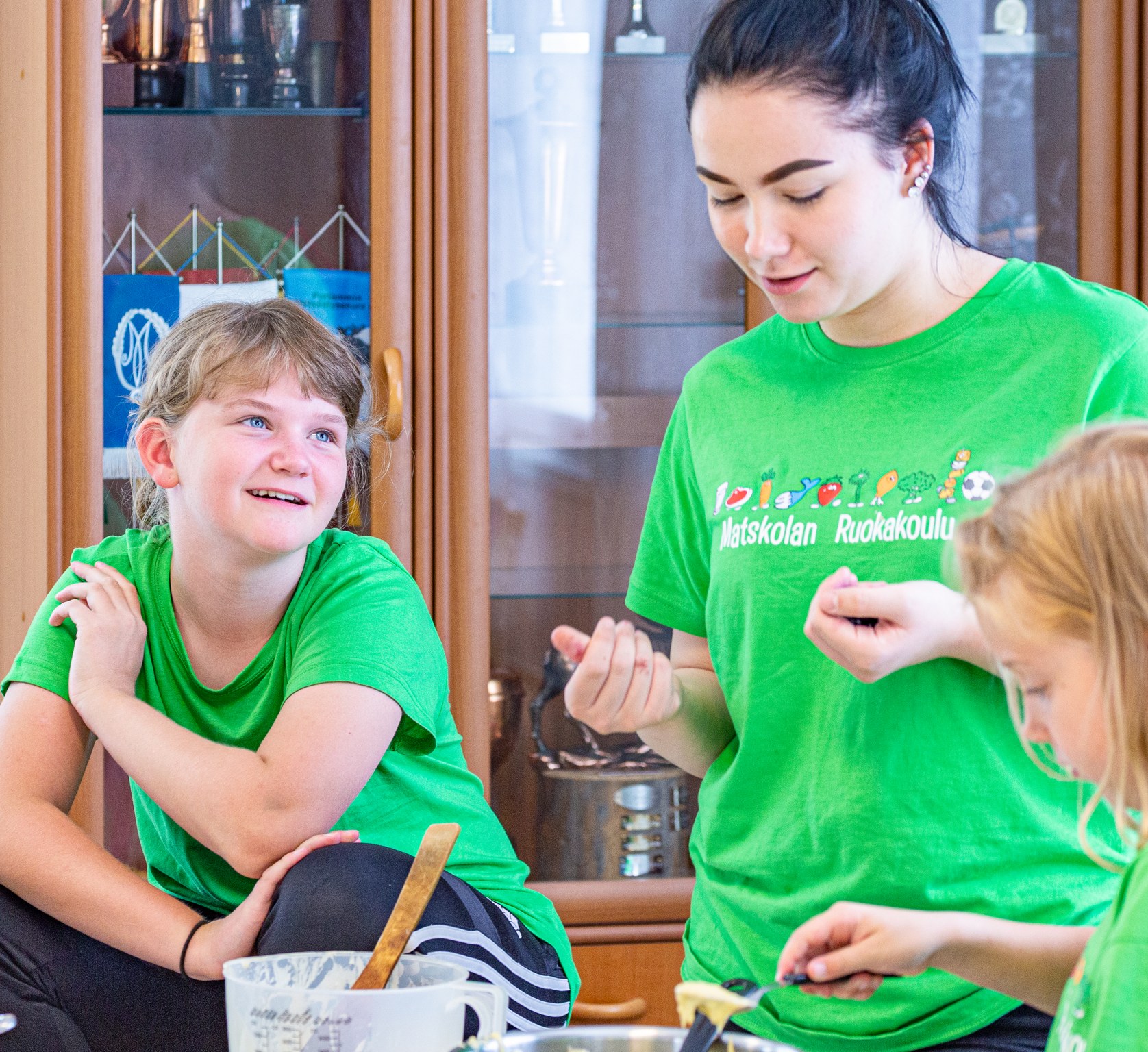 Kaksi lasta ja ohjaaja Ruokakoulussa vihreät Ruokakoulu t-paidat päällä