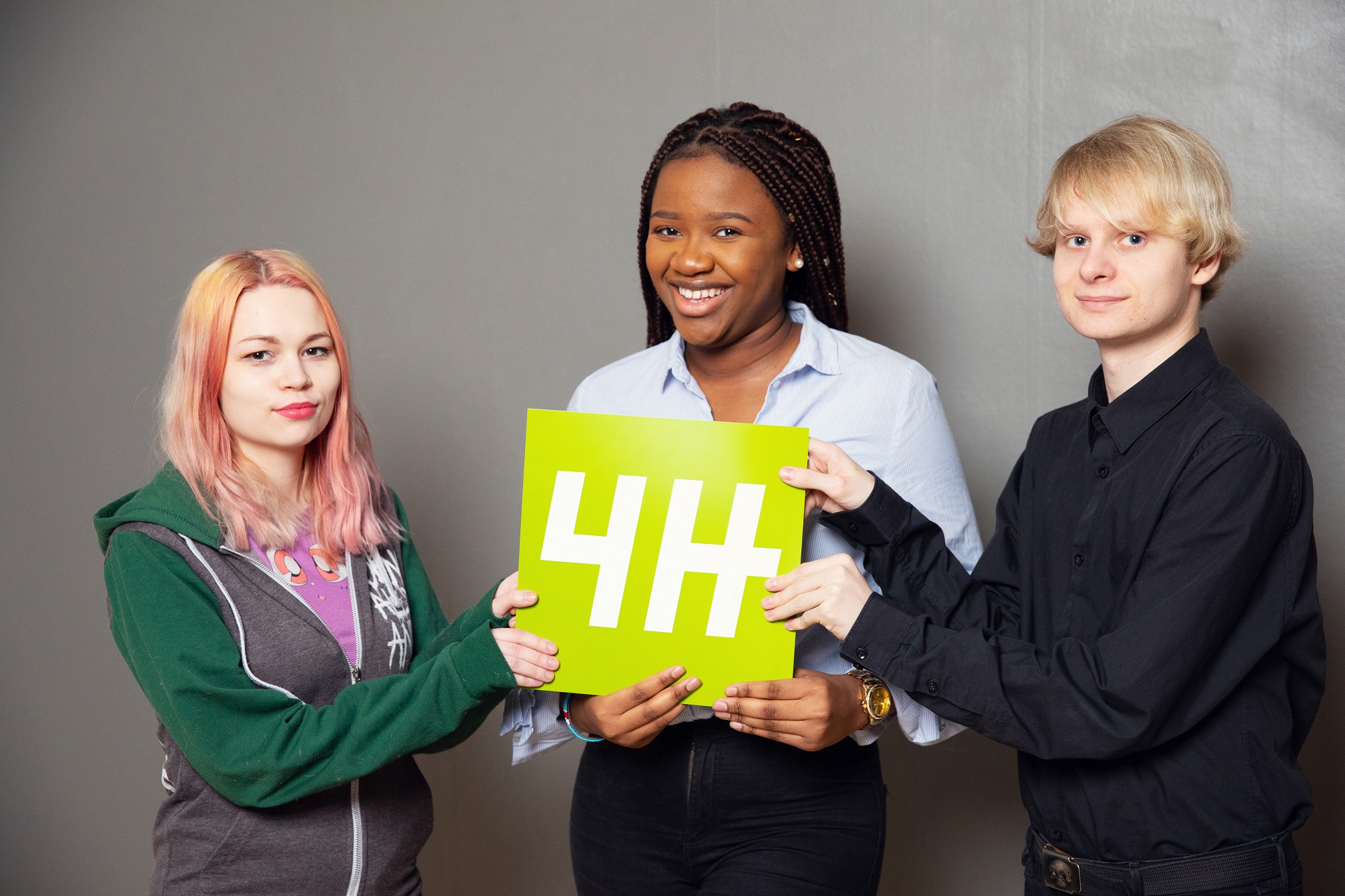 Kolme nuorta pitää yhdessä käsissään 4H-logoa