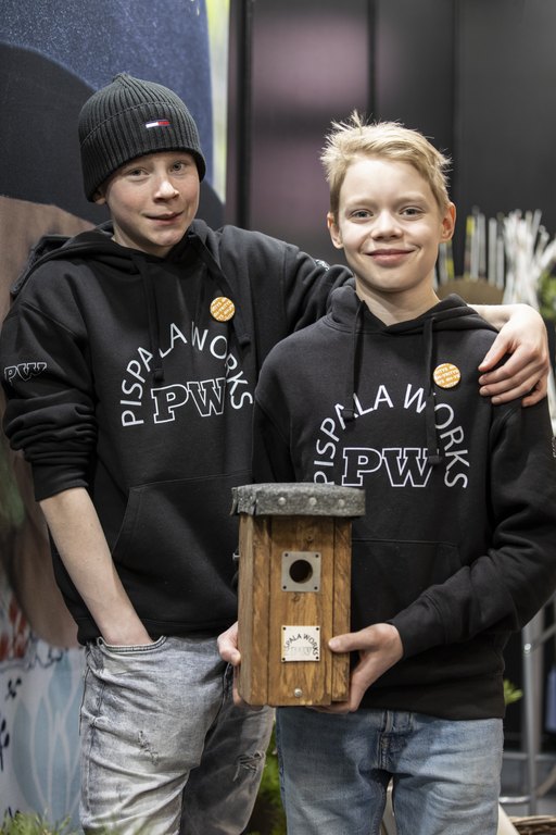 Kahdella yrittäjällä on päällään yrityksensä logopaidat ja kädessään linnunpönttö.