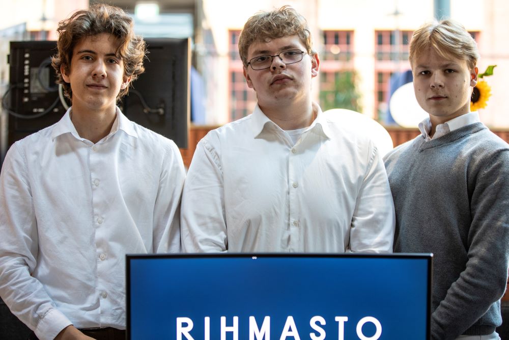 Kolme kauluspaitaan pukeutunutta poikaa seisoo näytön edessä, jossa lukee yrityksen nimi Rihmasto.